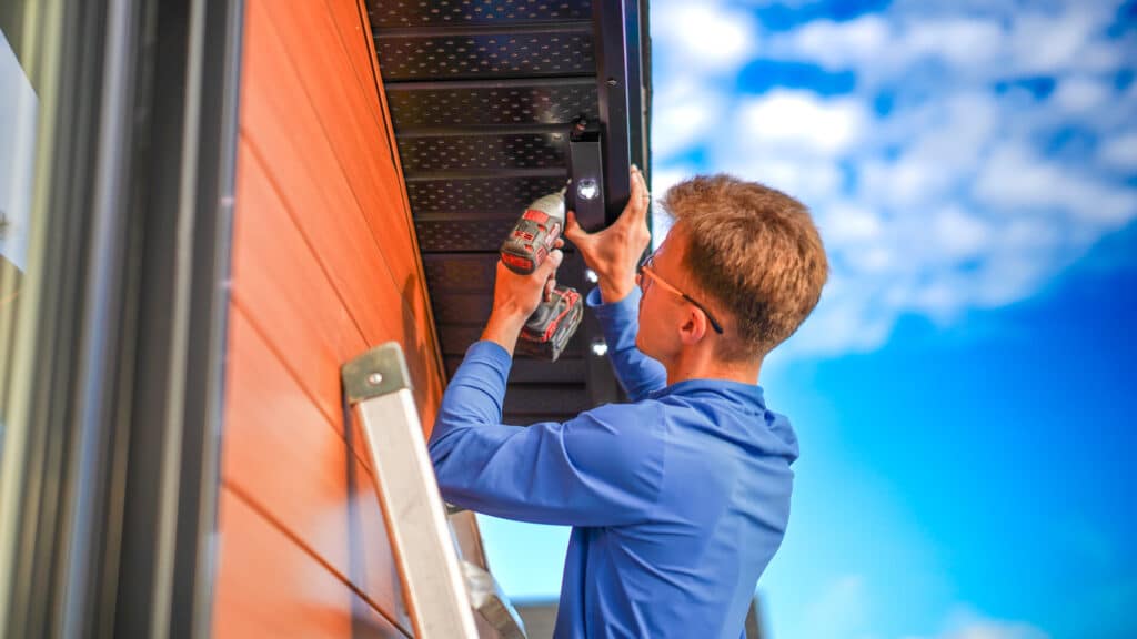 A professional installer mounting a permanent, color-changing LED lighting system along the roofline of a residential home in Redbridge, Ontario.