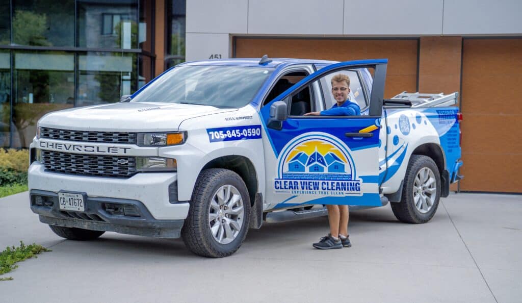 A branded Clear View Cleaning service vehicle parked at a residential property, with a uniformed technician arriving to greet the homeowner and confirm the project details.