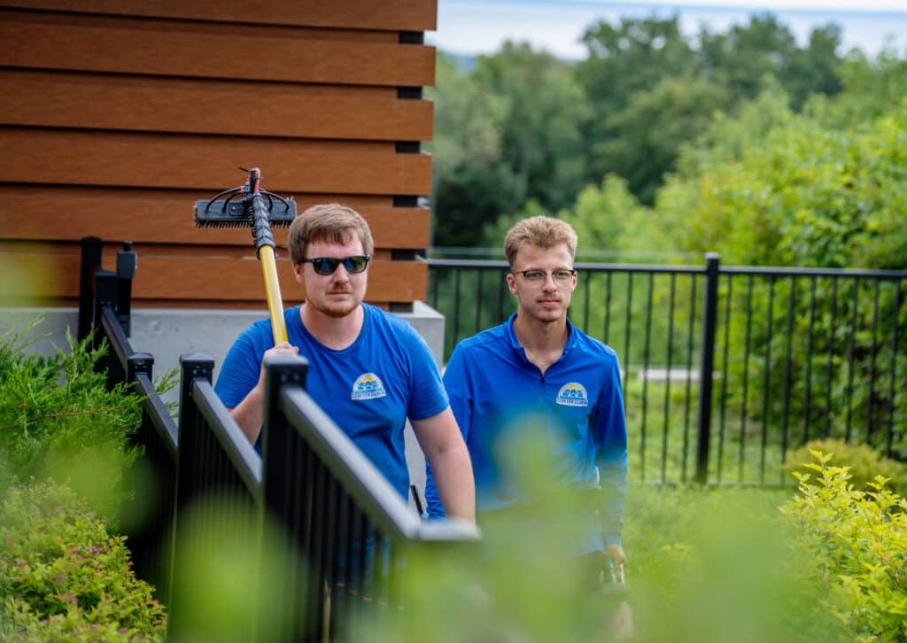 A Clear View Cleaning specialist performing a detailed exterior inspection of a home, checking for surface integrity and protecting nearby landscaping before the cleaning process begins.